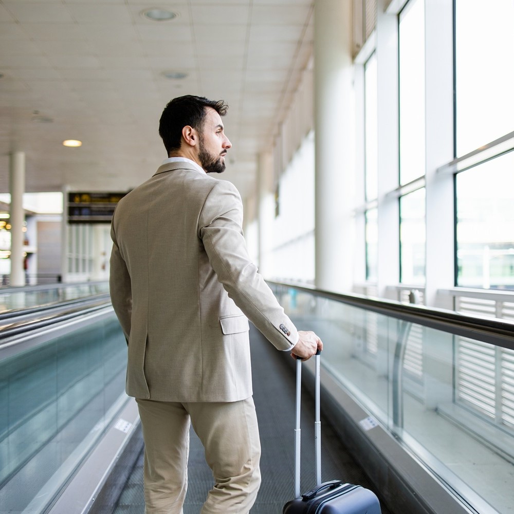 旅先でスーツケースを引きながら空を見ている男性